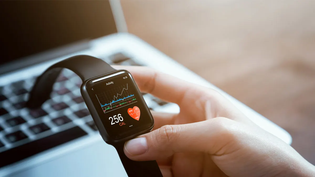 Eine Frau hält eine Smartwatch in der Hand. Darauf zu sehen sind eine Health-App mit Herz-Symbol und die Zahl 256 neben ein paar Graphen.