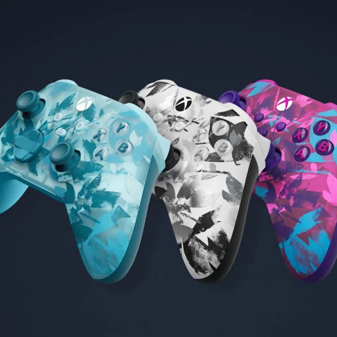 Drei Xbox‑Controller im Camouflage‑Design (türkis, schwarz‑weiß, pink/blau) nebeneinander, kabellose Controller mit Analogsticks, Steuerkreuz und A/B/X/Y‑Tasten.