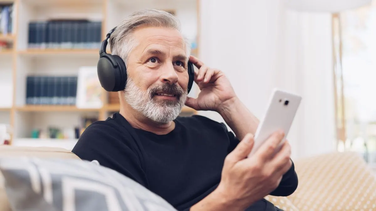 Ein Mann trägt Over-Ear-Kopfhörer und hält ein Smartphone in der Hand.