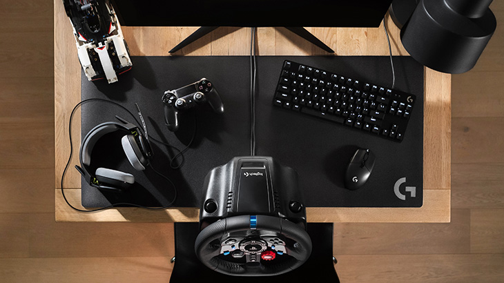 Auf einem Holztisch liegen Kopfhörer, ein Lenkrad, eine Maus, eine Tastatur, ein Controller und ein Spielzeugauto.