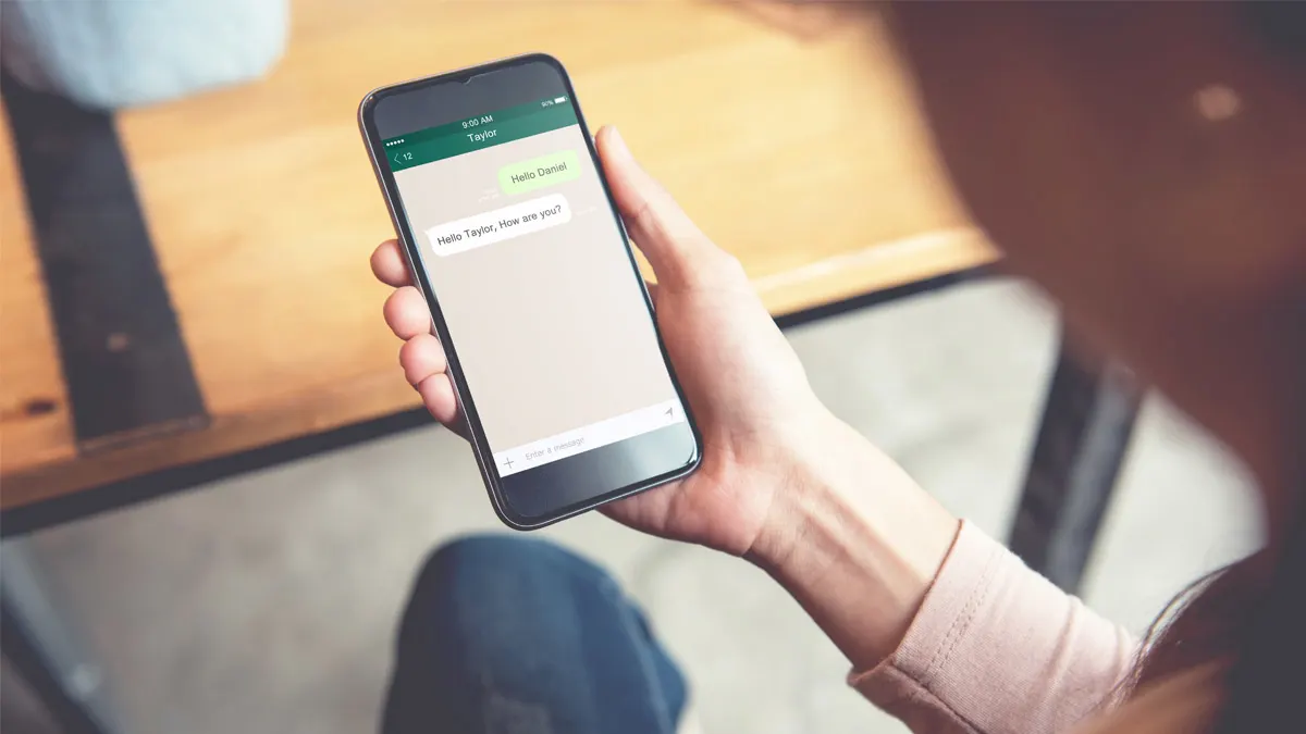 Eine Person hält ein Smartphone in der Hand. Darauf ist ein Chatverlauf zu sehen.