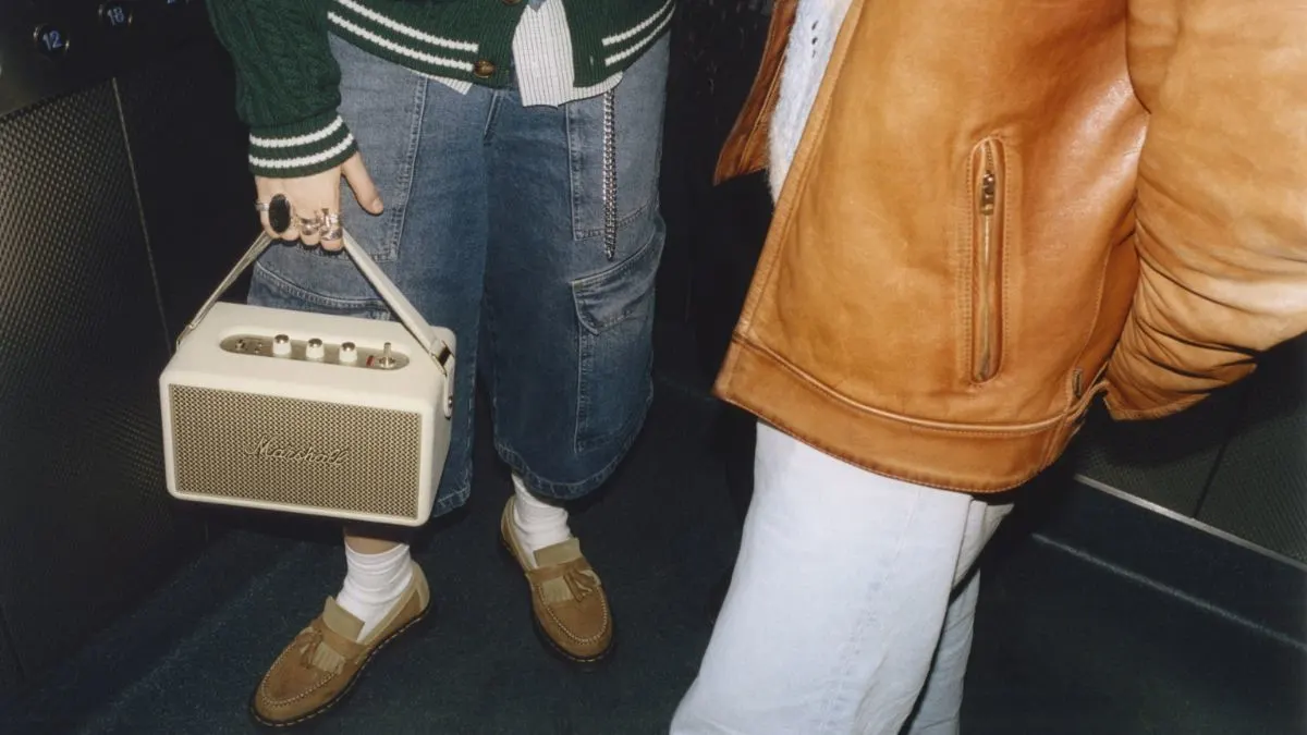 Zwei Personen mit Jeans, Lederjacke und Loafers im Aufzug. Eine Person trägt einen tragbaren Marshall-Lautsprecher.