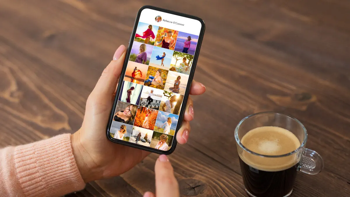 Hand hält ein Smartphone mit einer Galerie-App; daneben steht eine Tasse Kaffee auf einem Holztisch.