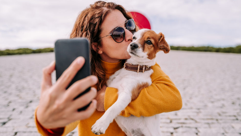 Frau küsst Hund und macht Selfie davon