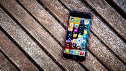 Ein iPhone SE mit einer roten Schutzhülle liegt auf einer Holzbank.
