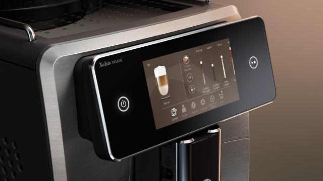 Nahaufnahme eines Kaffeevollautomaten mit Touchscreen-Bedienfeld, das Getränkeoptionen und Einstellungen anzeigt.
