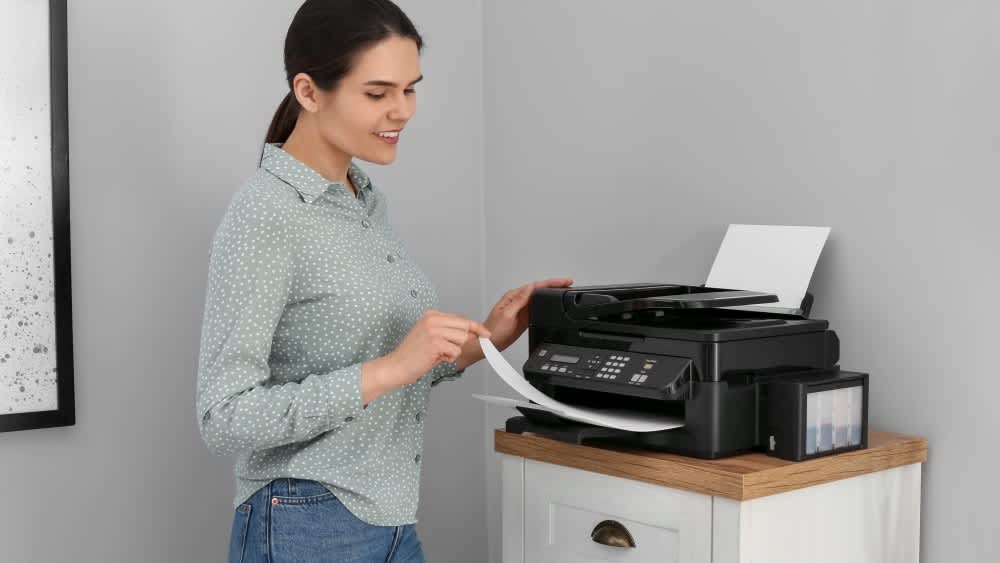 Eine Frau steht neben einem Drucker und zieht ein Blatt Papier raus.