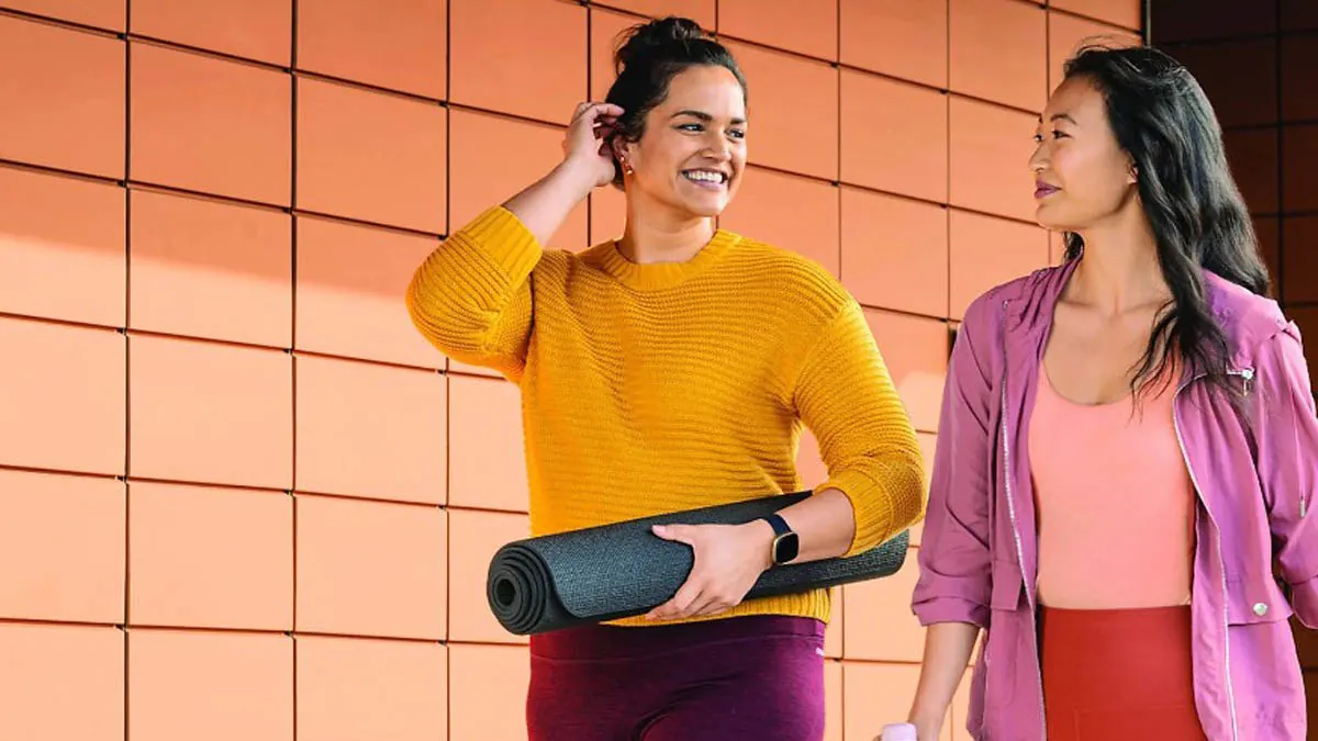 Zwei Frauen mit Yogamatte und Trinkflasche im Vorbeigehen. Eine trägt eine schwarze Fitbit Versa 3 am Handgelenk.