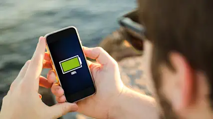 Eine Person hält ein Smartphone mit einem grünen Batteriesymbol, das 100 % Ladung anzeigt.