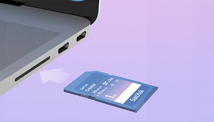 SanDisk SD‑Karte wird in den Kartenleser eines Laptops eingeschoben; Pfeil markiert den Slot neben zwei USB‑C‑Anschlüssen.