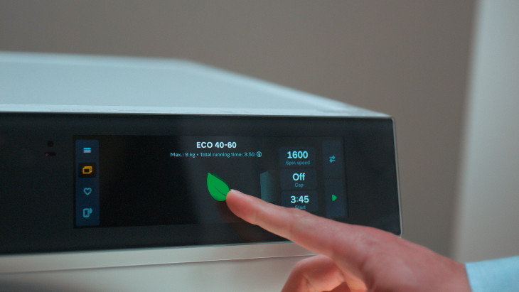 Ein Finger berührt ein grünes Blattsymbol auf dem Display einer Waschmaschine, das den ECO 40-60 Modus anzeigt.