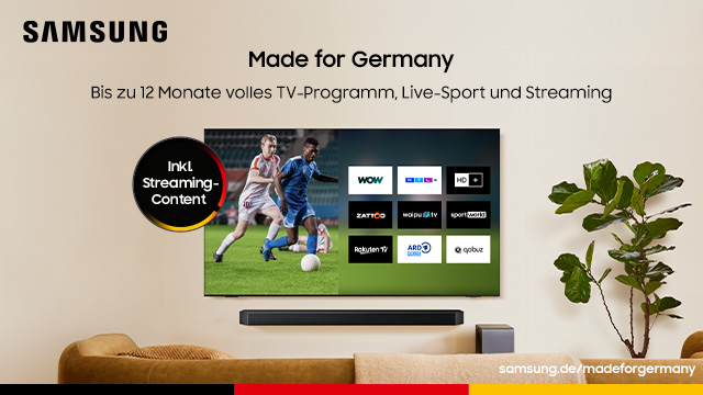 Ein modernes Wohnzimmer mit einer hölzernen TV-Kommode, darauf eine Soundbar. An der Wand hängt ein Samsung-Fernseher, auf dessen Bildschirm verschiedene Apps und TV-Sender wie Das Erste, ZDF, RTL, ProSieben, MagentaTV, Apple TV+, Disney+ und Netflix zu sehen sind. Über dem Fernseher steht der Schriftzug „Made for Germany“, oben rechts das Samsung-Logo. Unten im Bild sind die Farben der deutschen Flagge zu sehen.