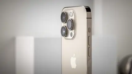 Ein goldenes Smartphone mit drei Kameralinsen auf der Rückseite und einem Apfel-Logo. Seitliche Tasten sind sichtbar.