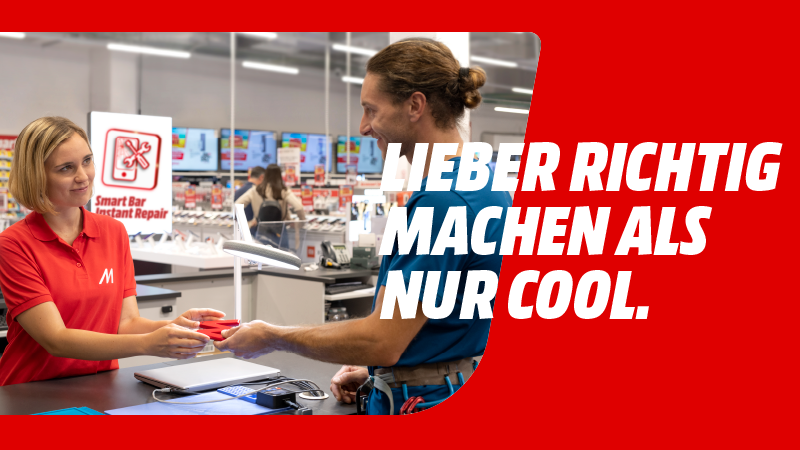 Eine Frau in rotem Hemd übergibt rote Gegenstände an einen Mann vor einem Ladentisch mit Laptop.