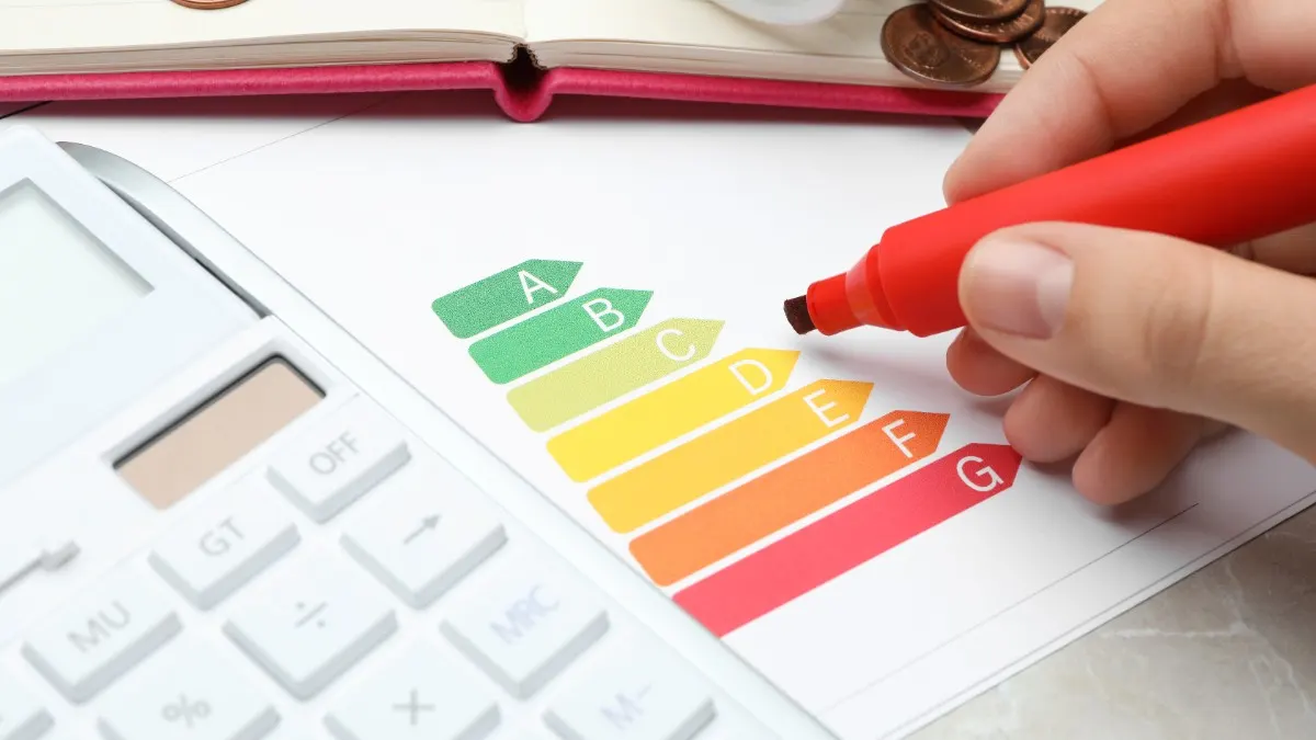 Eine Hand hält einen Markierstift über einem Energieeffizienzlabel, daneben liegt ein Taschenrechner.