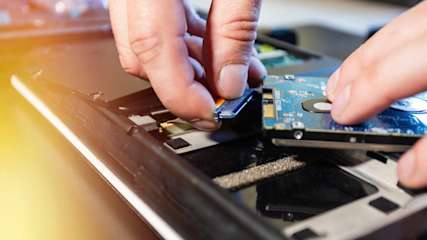 Eine Person baut eine Festplatte in einen Laptop ein.