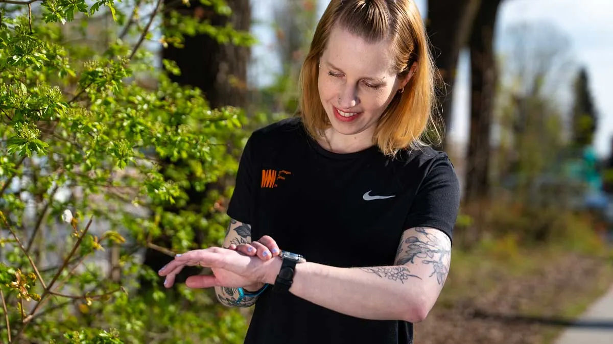 Franzi steht in Laufkleidung draußen und schaut lächelnd auf die Amazfit Active 3 Premium.