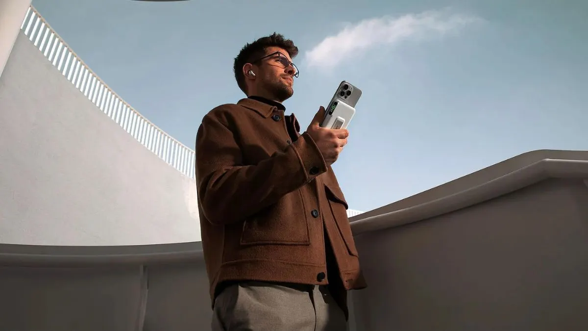 Ein Mann steht auf einem Balkon und hält ein Handy in der Hand, das von der induktiven Powerbank Anker MagGo aufgeladen wird.