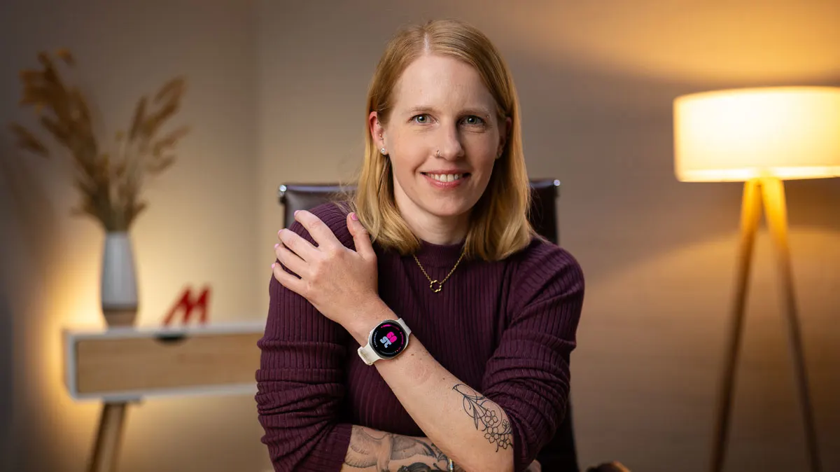 Franzi sitzt auf einem Schreibtischstuhl und hält ihren Arm mit der Samsung Galaxy Watch9 schräg vor dem Oberkörper.