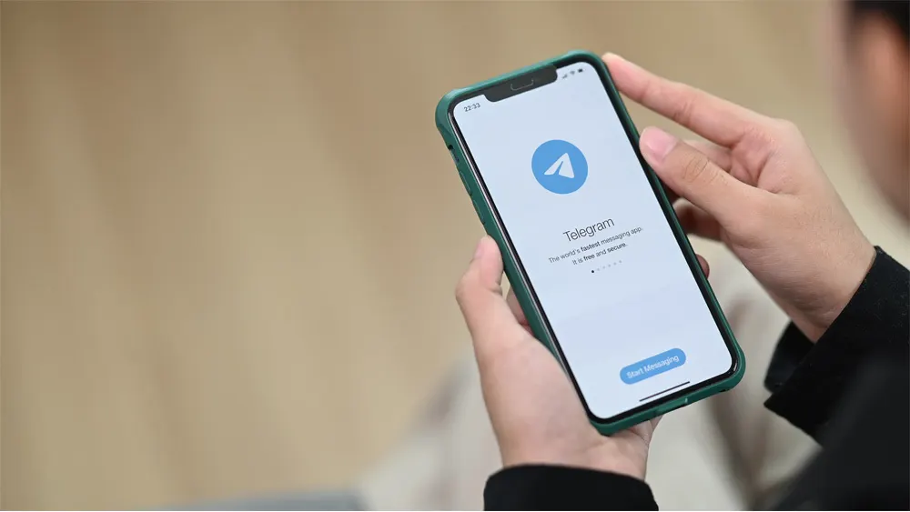 Eine Person hält ein Smartphone mit der Telegram-App in den Händen, wobei der Startbildschirm angezeigt wird.