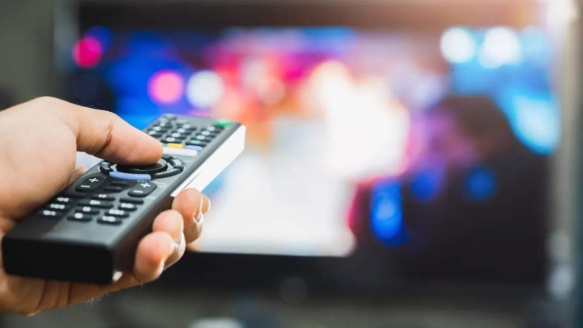Eine Person richtet eine Fernbedienung auf einen Fernseher.