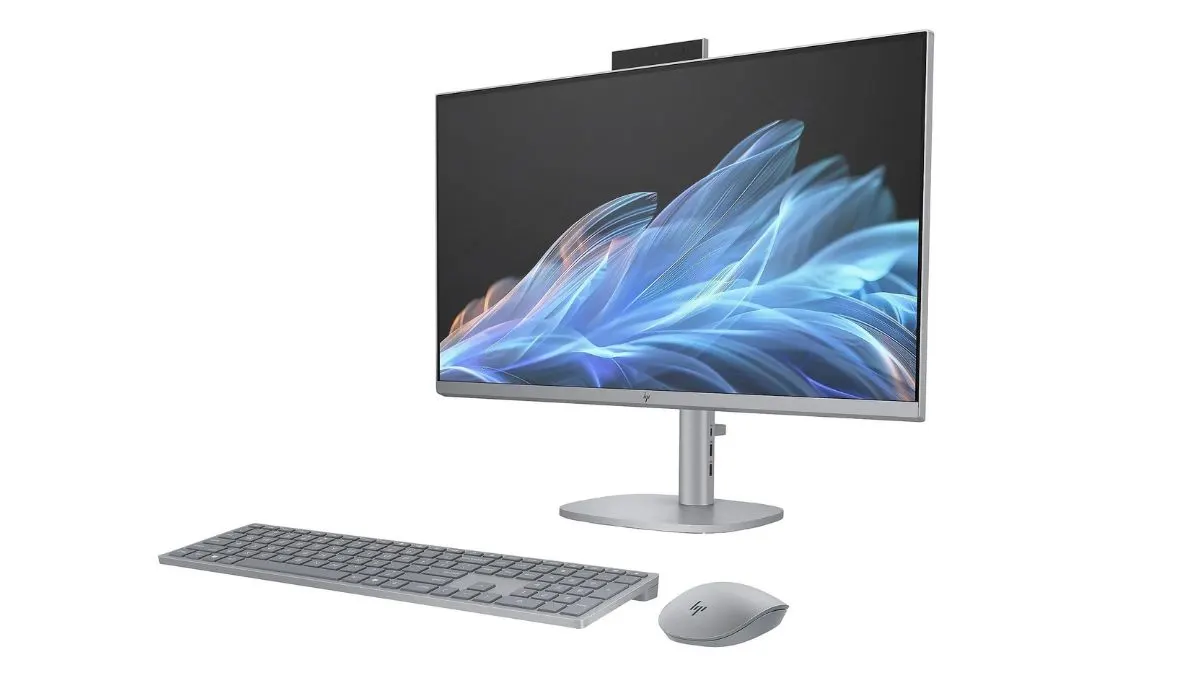 Silberner All-in-One-Computer mit Tastatur und Maus vor weißem Hintergrund. Auf dem Bildschirm sind blaue und weiße abstrakte Designs.