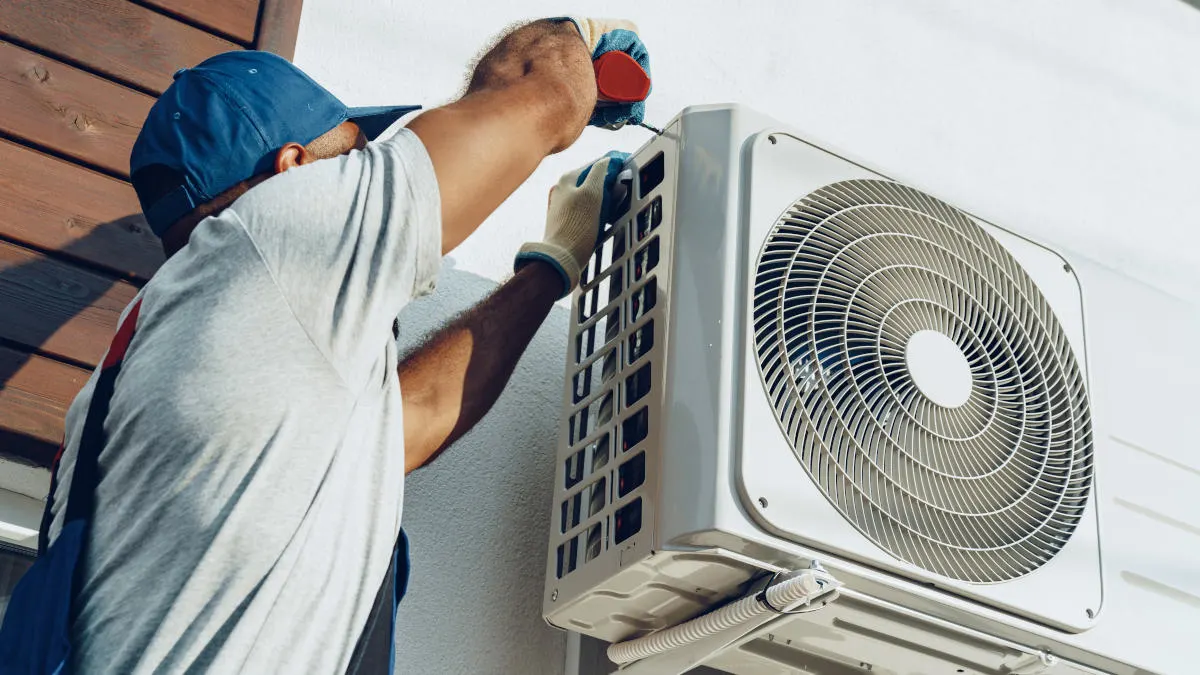 Ein Mann installiert die Außeneinheit einer Split-Klimaanlage an einer Hauswand..