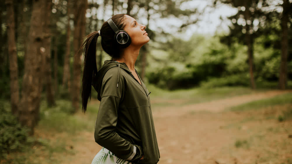 Frau hört über Bluetooth-Over-Ear-Kopfhörer Musik im Wald
