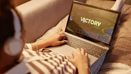 Person mit Kopfhörern spielt ein Spiel auf einem Laptop mit dem Wort „Victory“ auf dem Bildschirm.