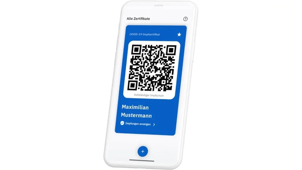 Ein weißes Smartphone zeigt ein blaues COVID-19-Impfzertifikat mit einem QR-Code und dem Namen Maximilian Mustermann.