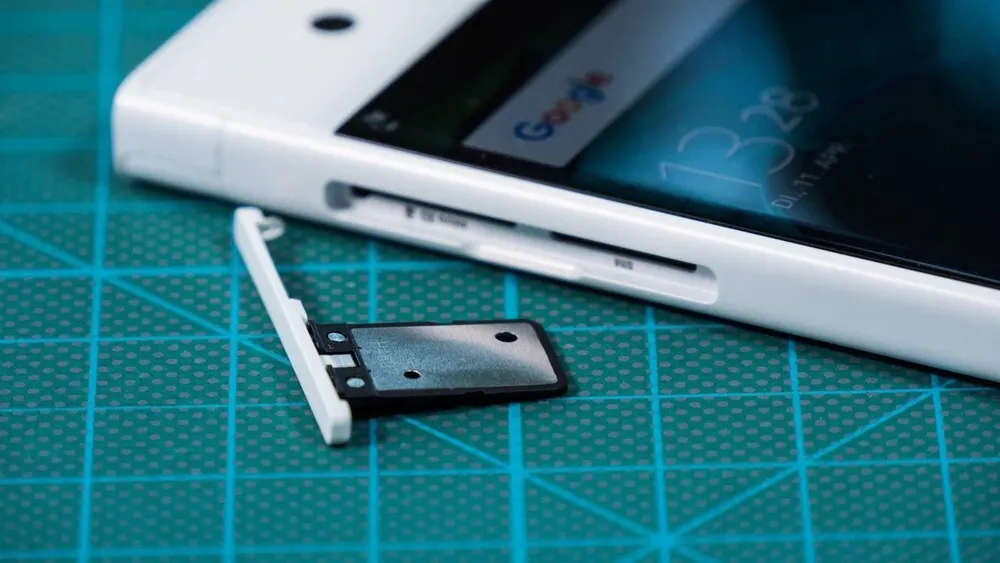 Ein weißes Smartphone liegt auf einer grünen Schneidematte, SIM-Karten-Slot ist offen und leer.