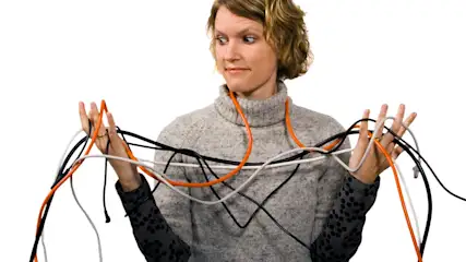 Eine Person im grauen Pullover hält mehrere orange, schwarze und weiße Kabel in ihren Händen vor einem weißen Hintergrund.