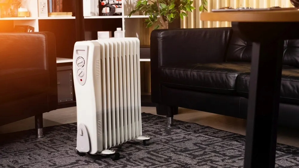 Ein weißer Heizkörper steht auf einem gemusterten Teppich, flankiert von einem schwarzen Ledersofa und einem Regal.