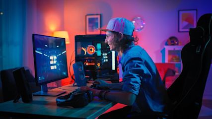 Ein lächelnder Mann sitzt vor einem PC und zockt.