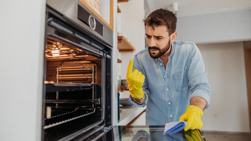 Mann reinigt Ofen mit gelben Putzhandschuhen