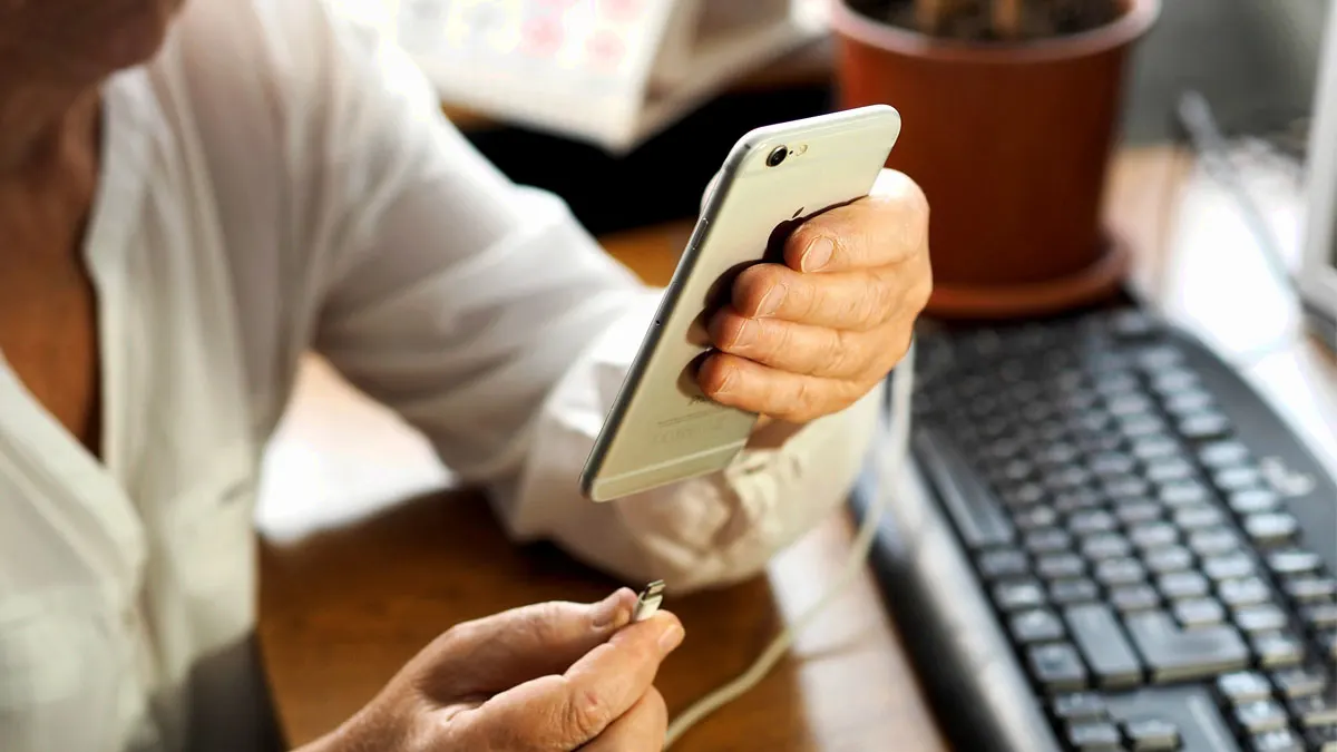 Frau vor einem Schreibtisch steckt gerade ihr Smartphone am Ladekabel an.