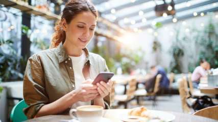 Eine Frau sitzt in einem Cafe und schaut auf ihr Smartphone.