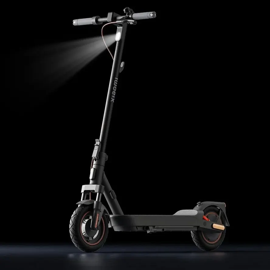 XIAOMI Electric Scooter 5 Max in seitlicher Ansicht vor schwarzem Hintergrund, Vorderlicht eingeschaltet, modernes schwarzes Design mit orangefarbenen Akzenten.