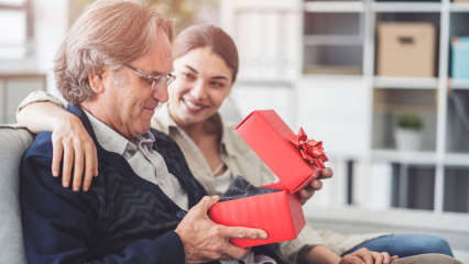 Ein Mann sitzt auf dem Sofa neben einem jüngeren Mädchen und öffnet ein Geschenk.
