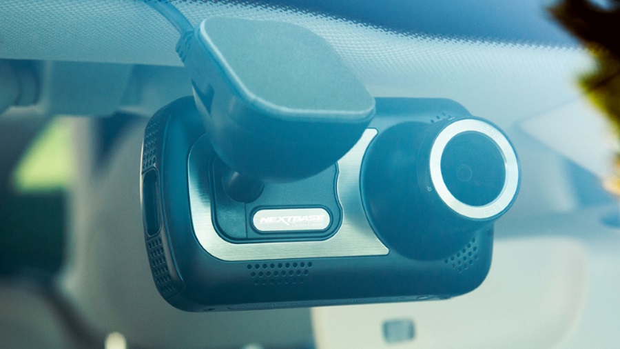 Eine schwarze Dashcam ist an einer Windschutzscheibe befestigt, wobei das Objektiv deutlich sichtbar ist. Ein Kabel ist angeschlossen.