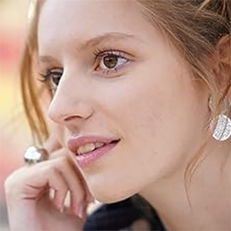 Frau mit silbernen Ohrringen und Ring. Ihre Hand berührt ihr Gesicht. Unschärfer Hintergrund mit hellen Farbtönen.