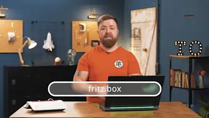 TURN ON Moderator Jens steht vor einem offenen Laptop, daneben steht eine Fritzbox.