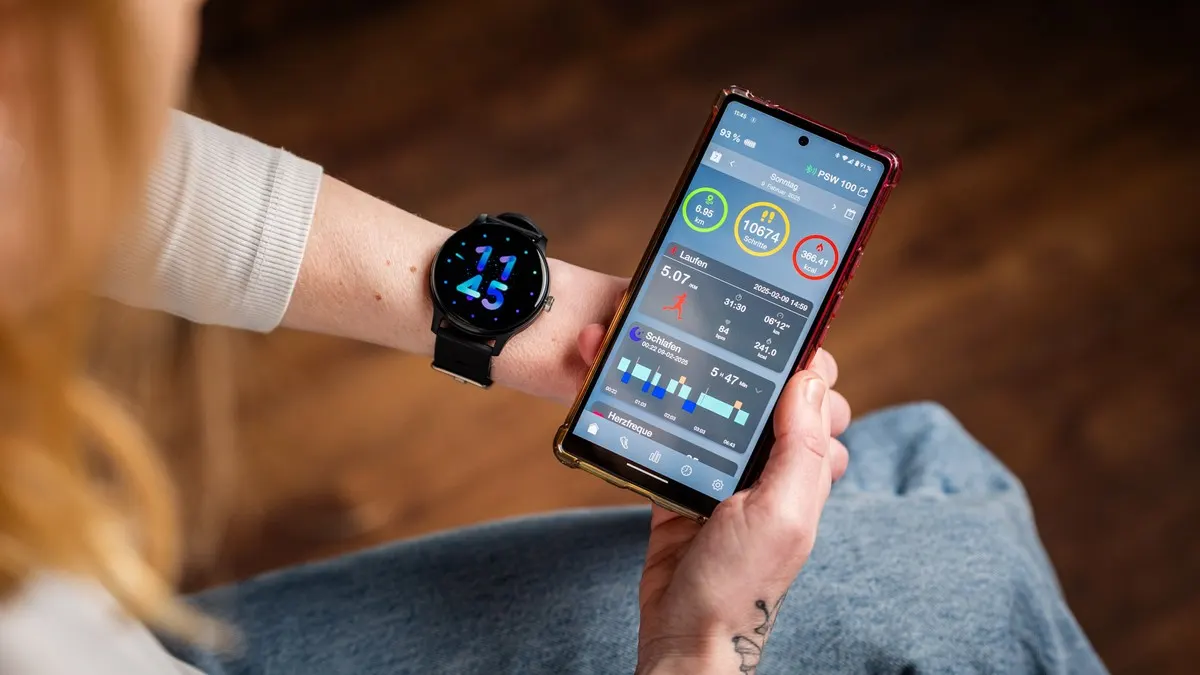 Person mit Smartwatch am Handgelenk und Smartphone, das Fitnessdaten auf dem Bildschirm anzeigt.