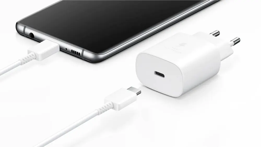 Schwarzes Smartphone mit weißem Ladekabel und Netzteil auf weißem Hintergrund. Das Kabel ist mit dem Telefon verbunden.