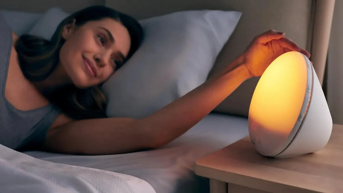 Eine im Bett liegende Frau berührt mit einer Hand den Rand des Lichtweckers Philips HF3531/01 auf ihrem Nachttisch.