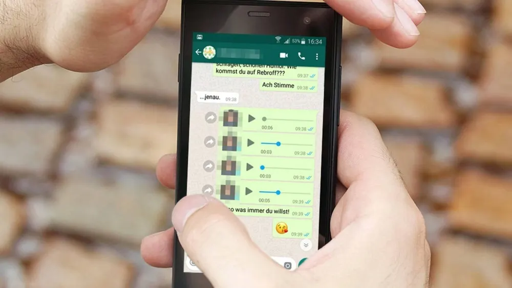 Eine Person hält ein Smartphone mit geöffnetem WhatsApp-Chat vor einem Backsteinhintergrund.