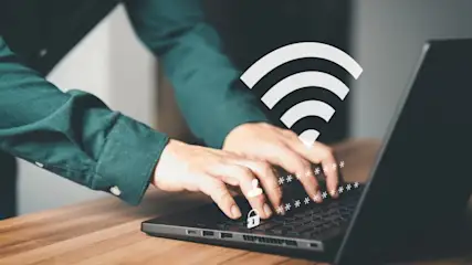 Eine Person tippt auf einem Laptop, mit WLAN-Symbol, Sternchen-Passwort und Schloss-Symbol auf der Tastatur.