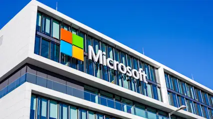 Fassade eines Bürogebäudes mit dem Microsoft-Logo und einem bunten Quadrat aus Orange, Grün, Blau und Gelb unter blauem Himmel.
