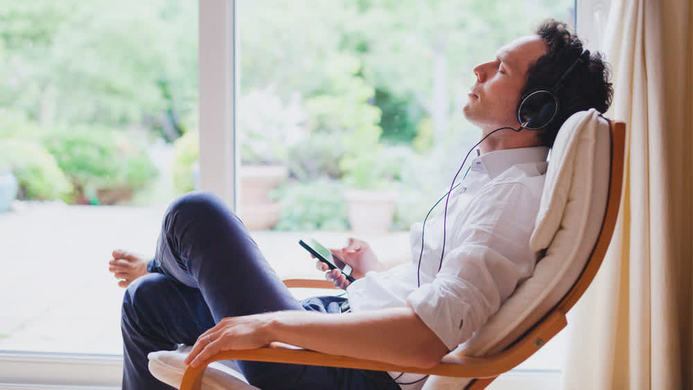 Ein Mann sitzt in einem Sessel und hört Musik vom Smartphone über Kopfhörer.
