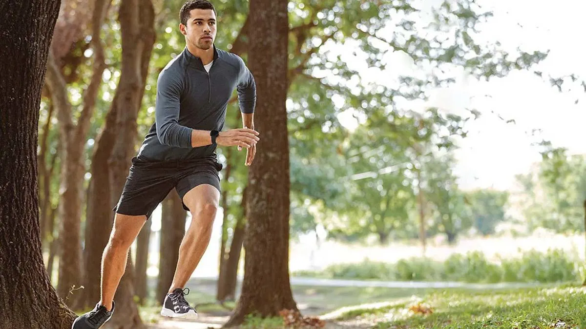 Ein Mann beim Joggen zwischen Bäumen mit einer Fitbit Versa 3 am Handgelenk.